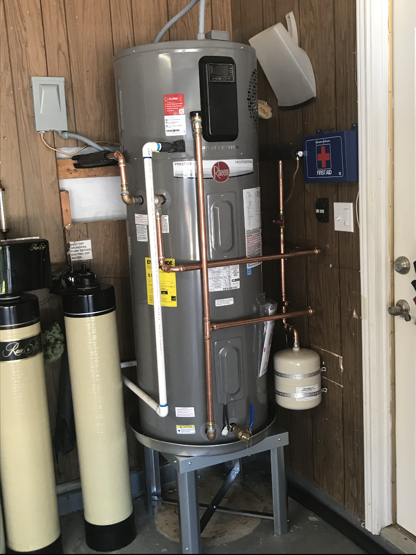 Water heater and water treatment system in a garage. Grey water heater with copper pipes and two tan tanks.