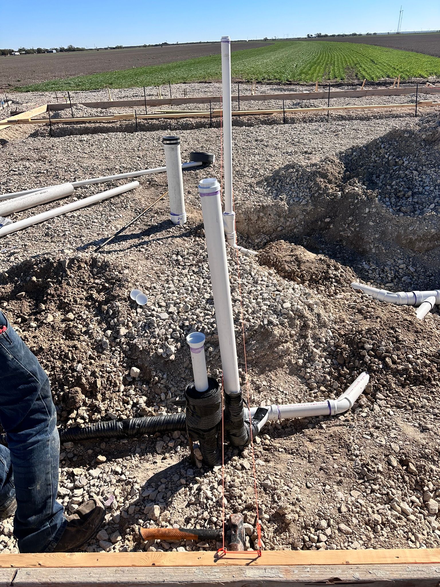 Plumbing pipes and gravel at a construction site. A person stands near the work.
