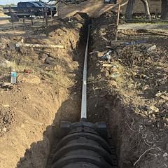 Trench with buried septic tank and pipe, outdoors near a house.