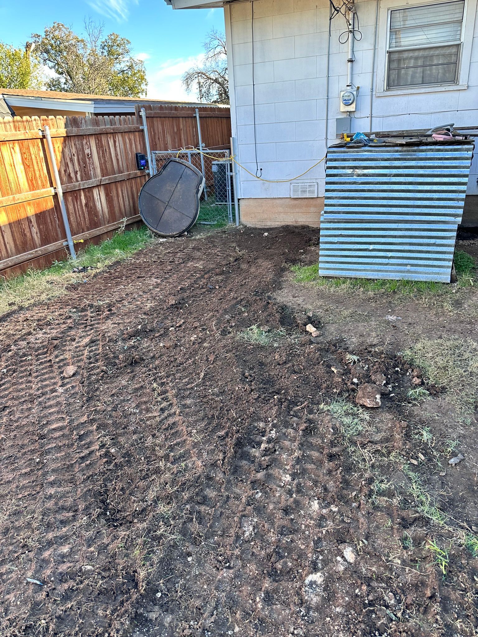 Dirt path in a yard next to a building. Rusty fence on the left. Blue sky.