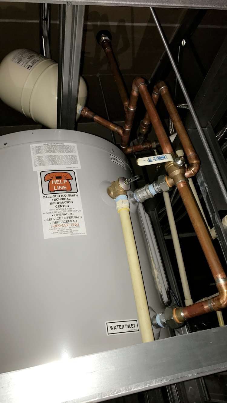 Copper pipes connected to a water heater and expansion tank in an indoor setting.