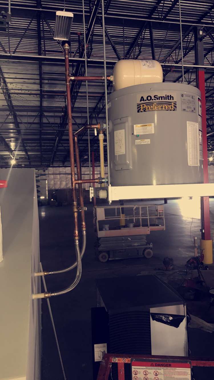 Copper pipes, a water heater, and a work light mounted in a warehouse.
