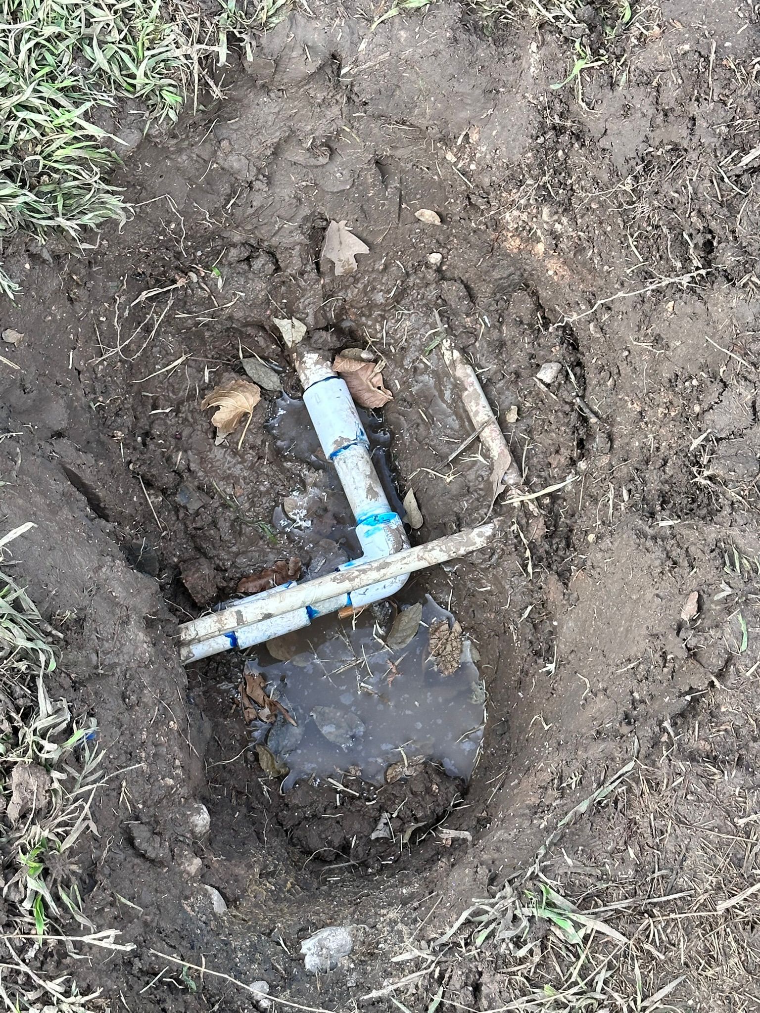 A hole in the ground containing irrigation pipes, surrounded by dirt and grass.