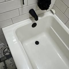 White bathtub with black faucet, drain and stopper. Tile wall.