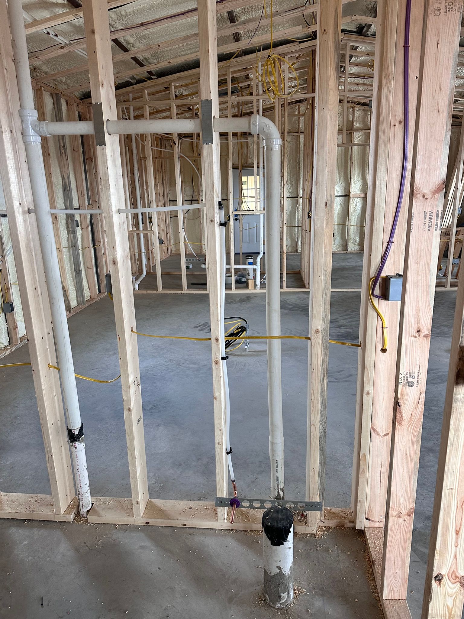 Framing of a room with grey plumbing pipes and electrical wiring installed.