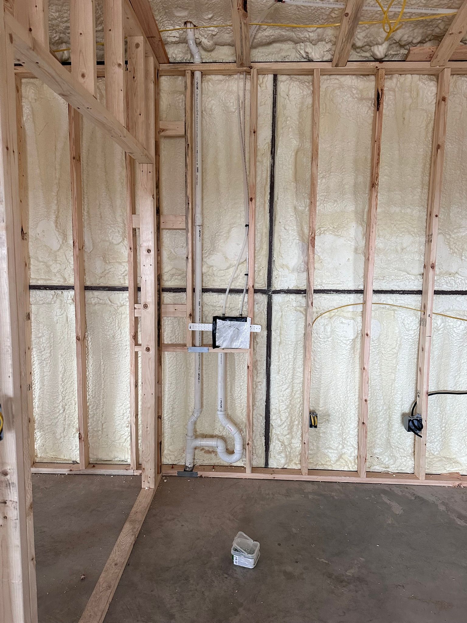 Interior of a room under construction; wooden studs, foam insulation, and plumbing visible.