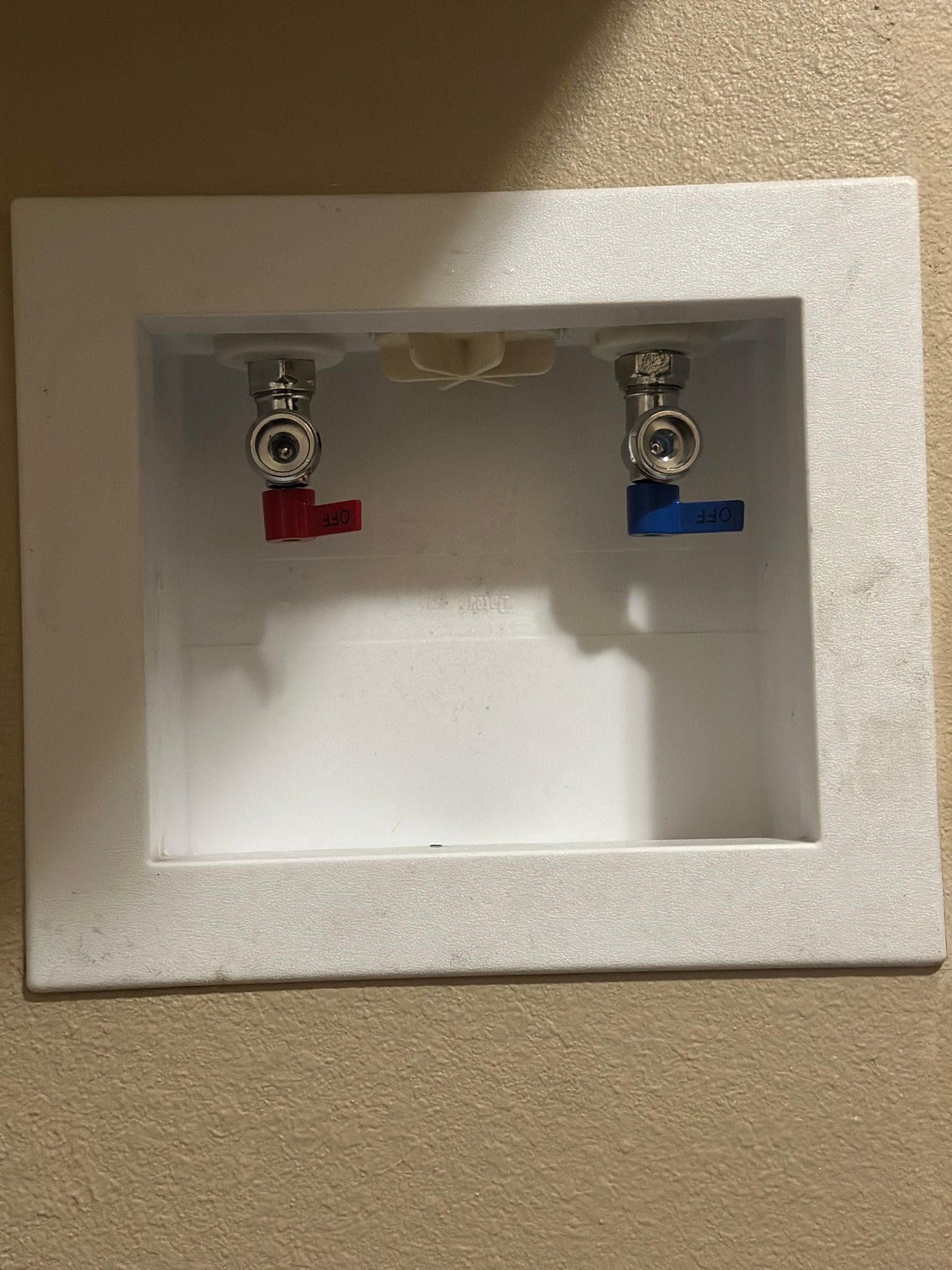 White laundry box with red and blue water shutoff valves.