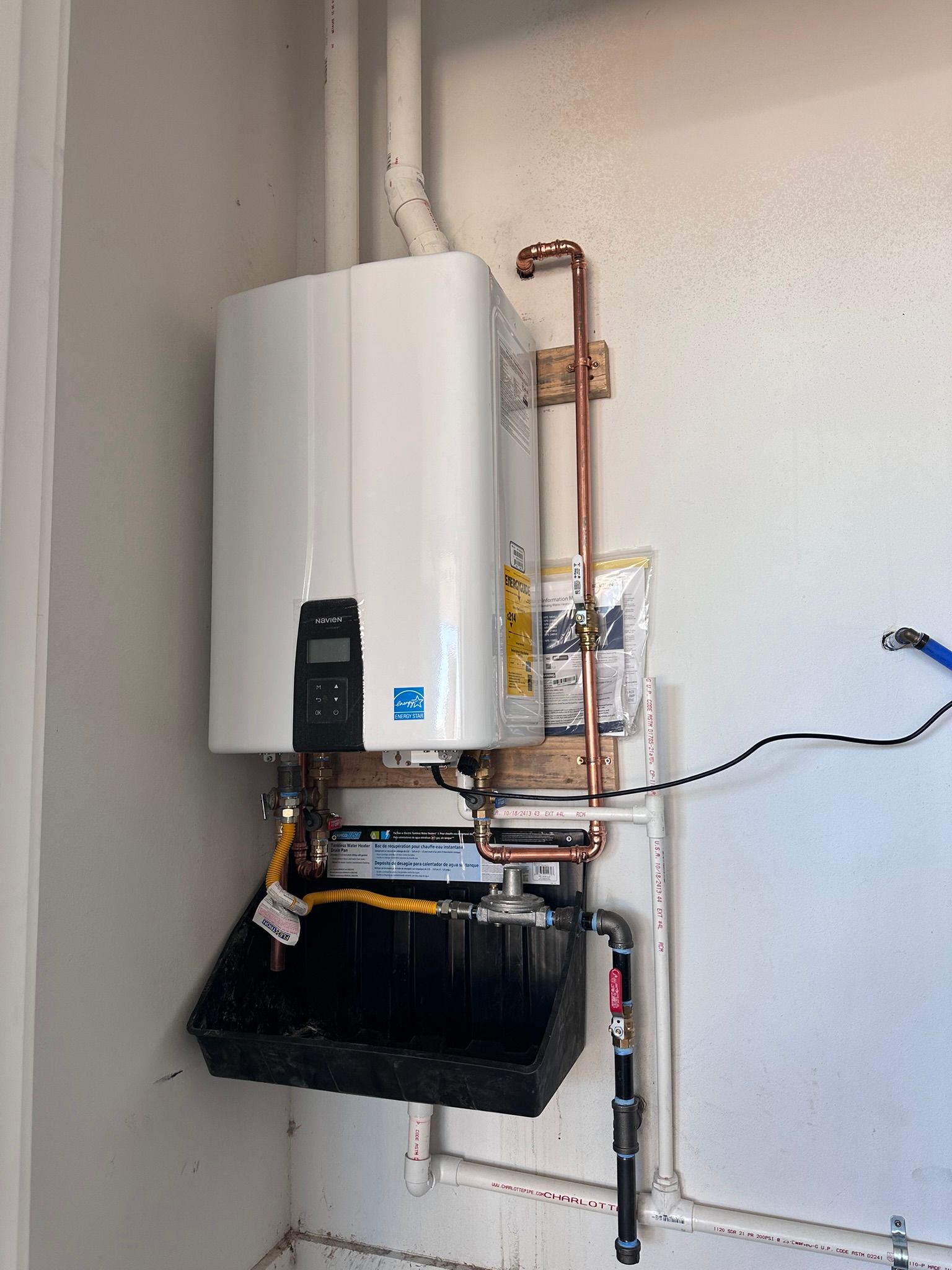 White wall-mounted tankless water heater with copper pipes and black drain pan.