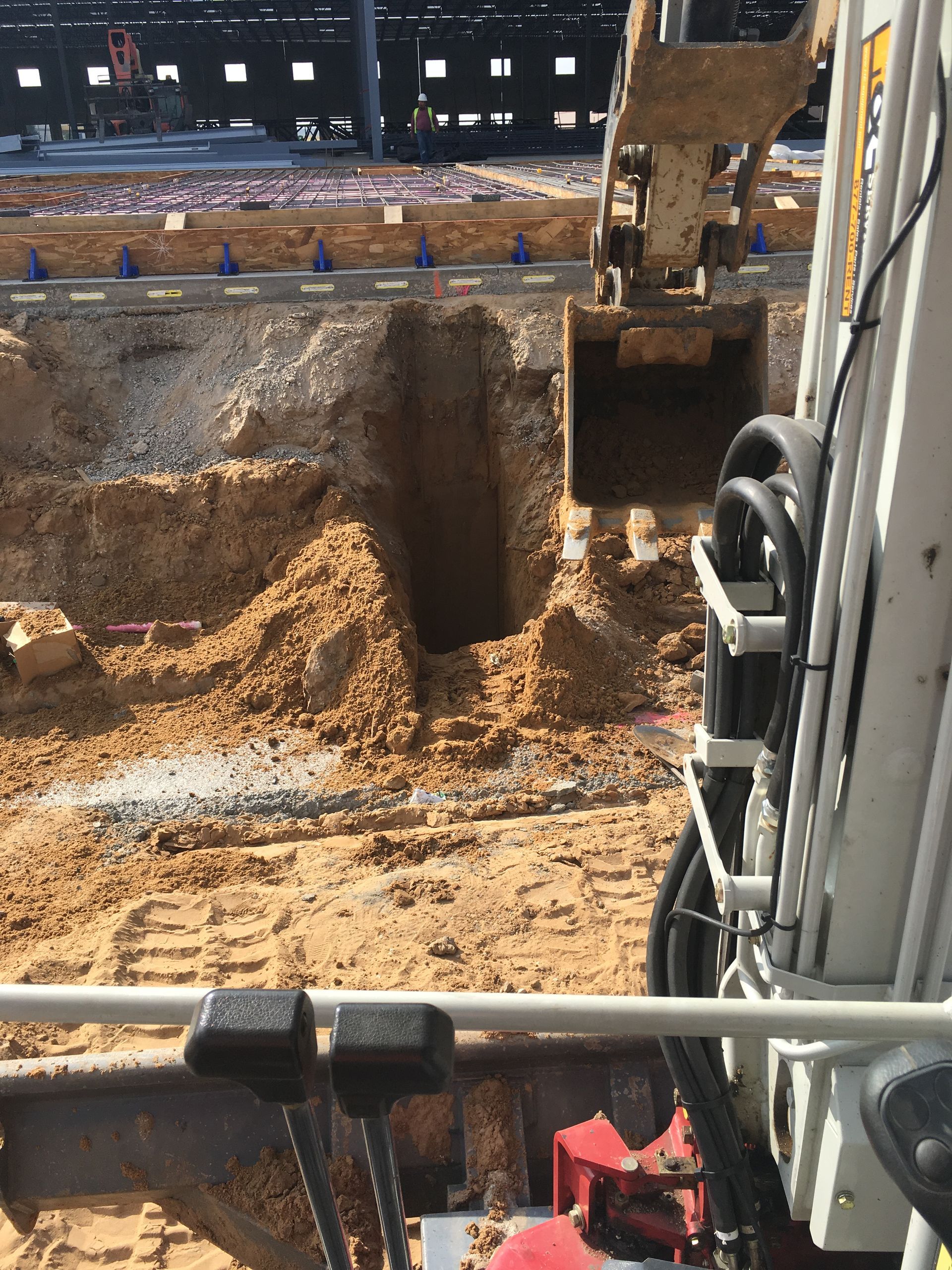 Excavator digging a trench on a construction site. Beige soil and metal construction visible.