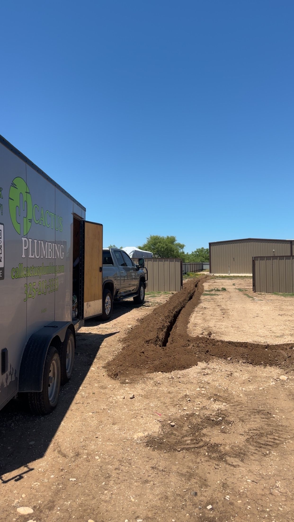 A trailer, truck, and mulch bed on dirt under a clear, blue sky.