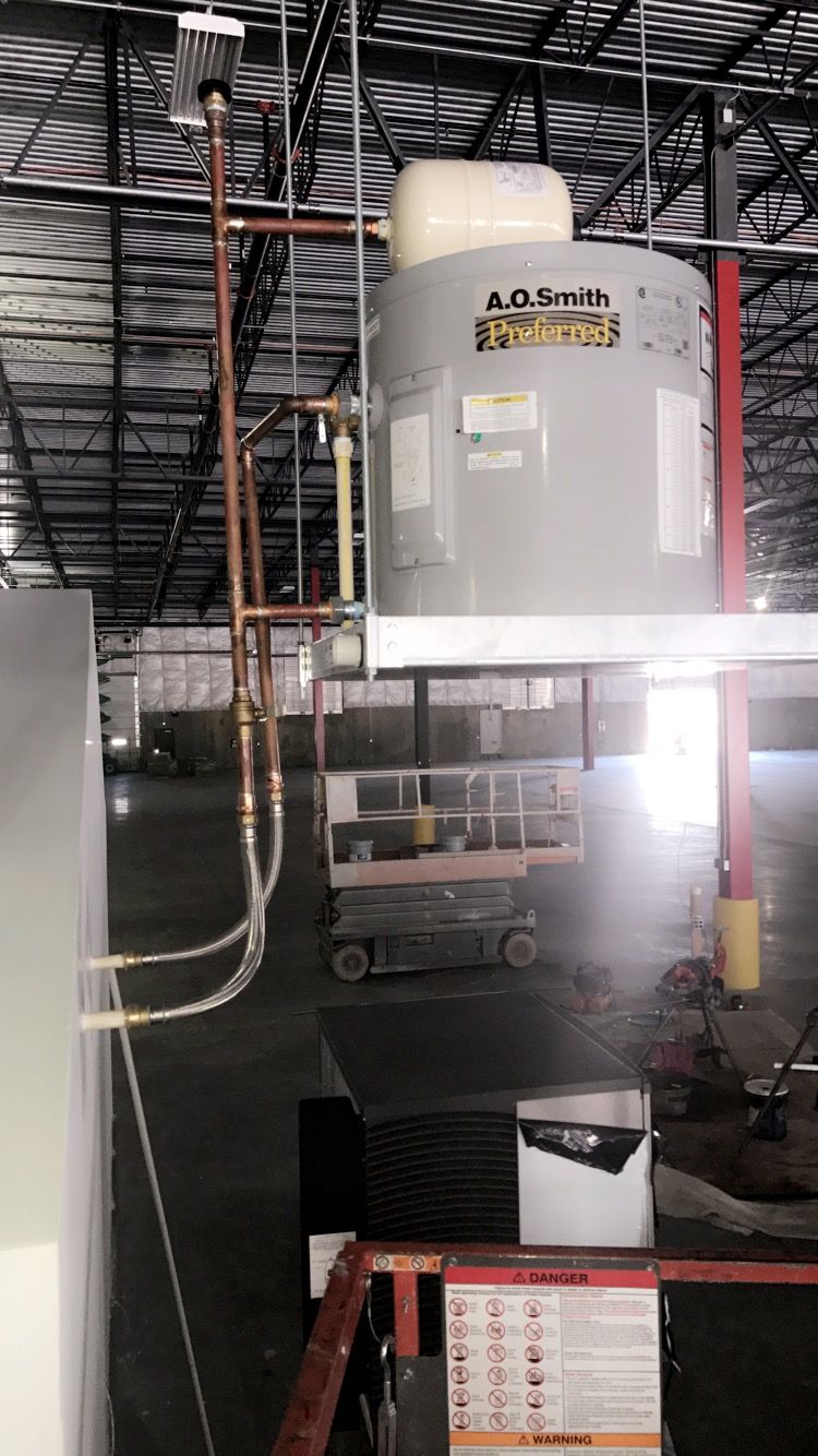 Water heater installation in a warehouse with copper pipes, on a scissor lift.
