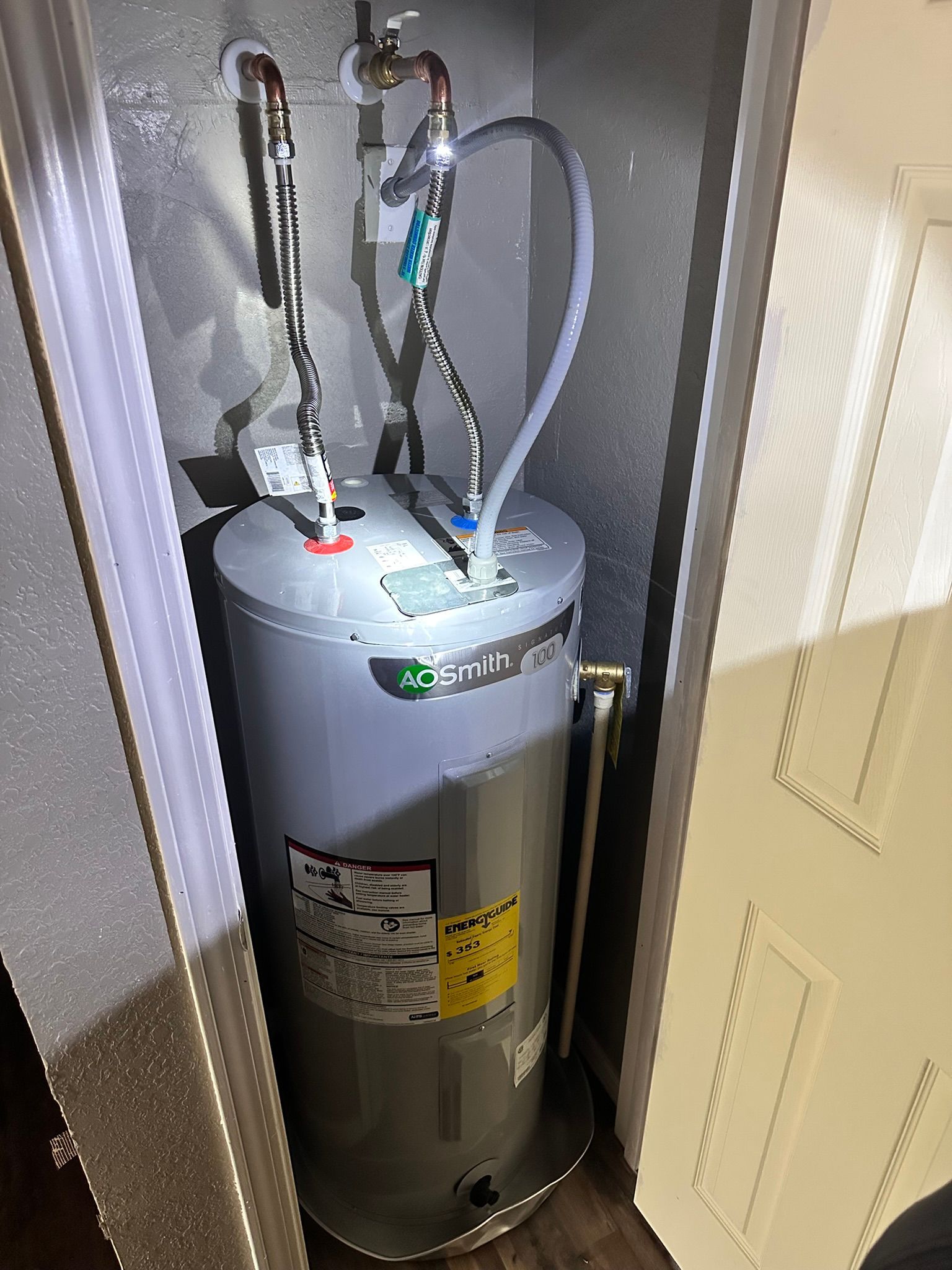 A water heater in a small closet, with water lines and a relief tube.