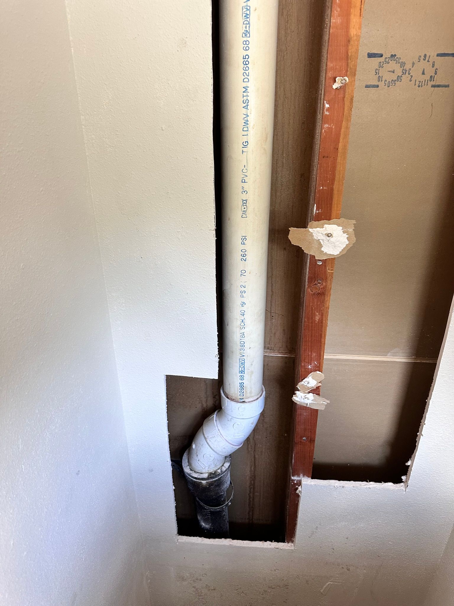 A white PVC pipe, bent at an angle, runs through an opening in a wall.