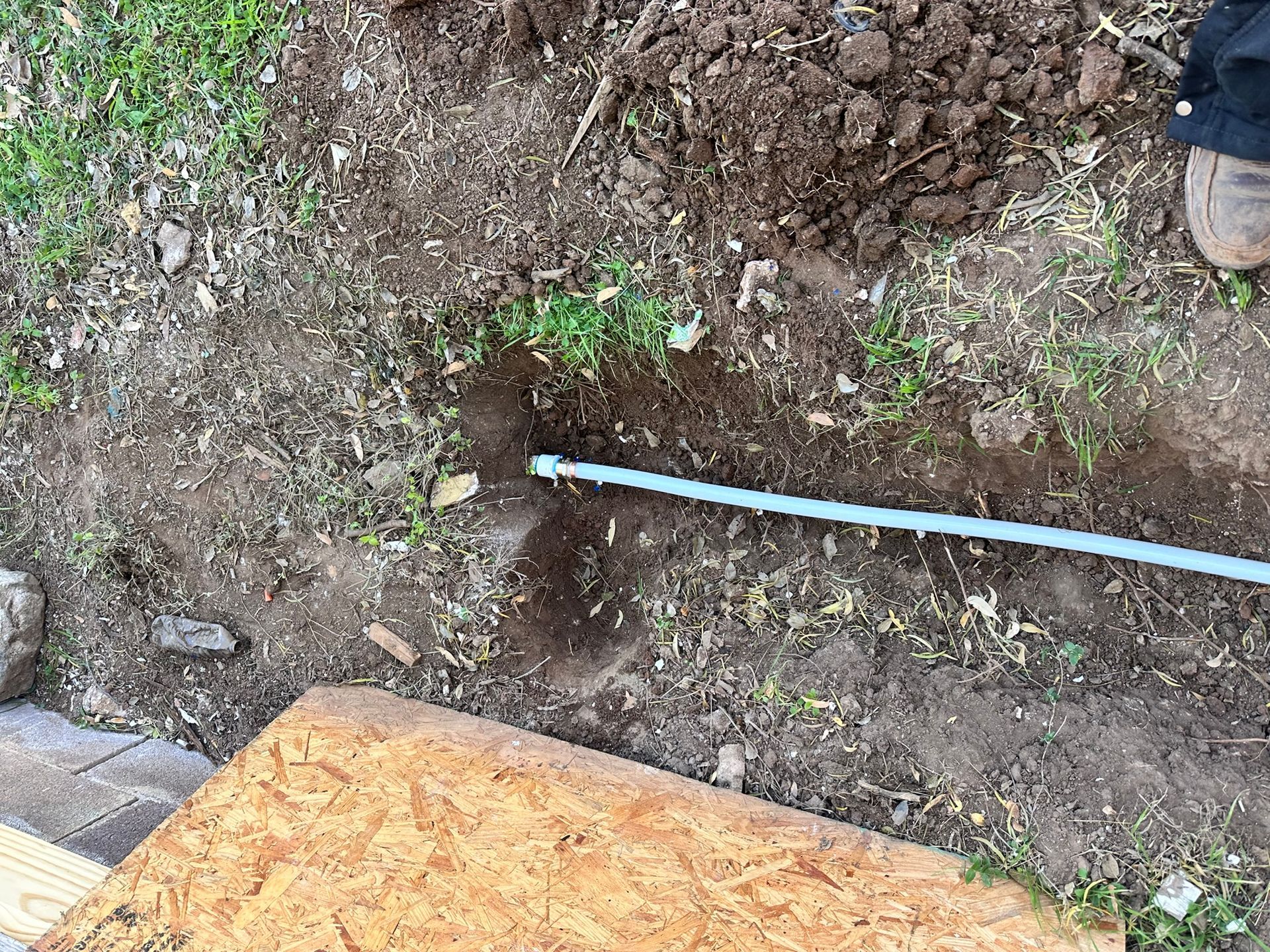 Blue pipe in a dirt trench outdoors near a wooden board and grass.