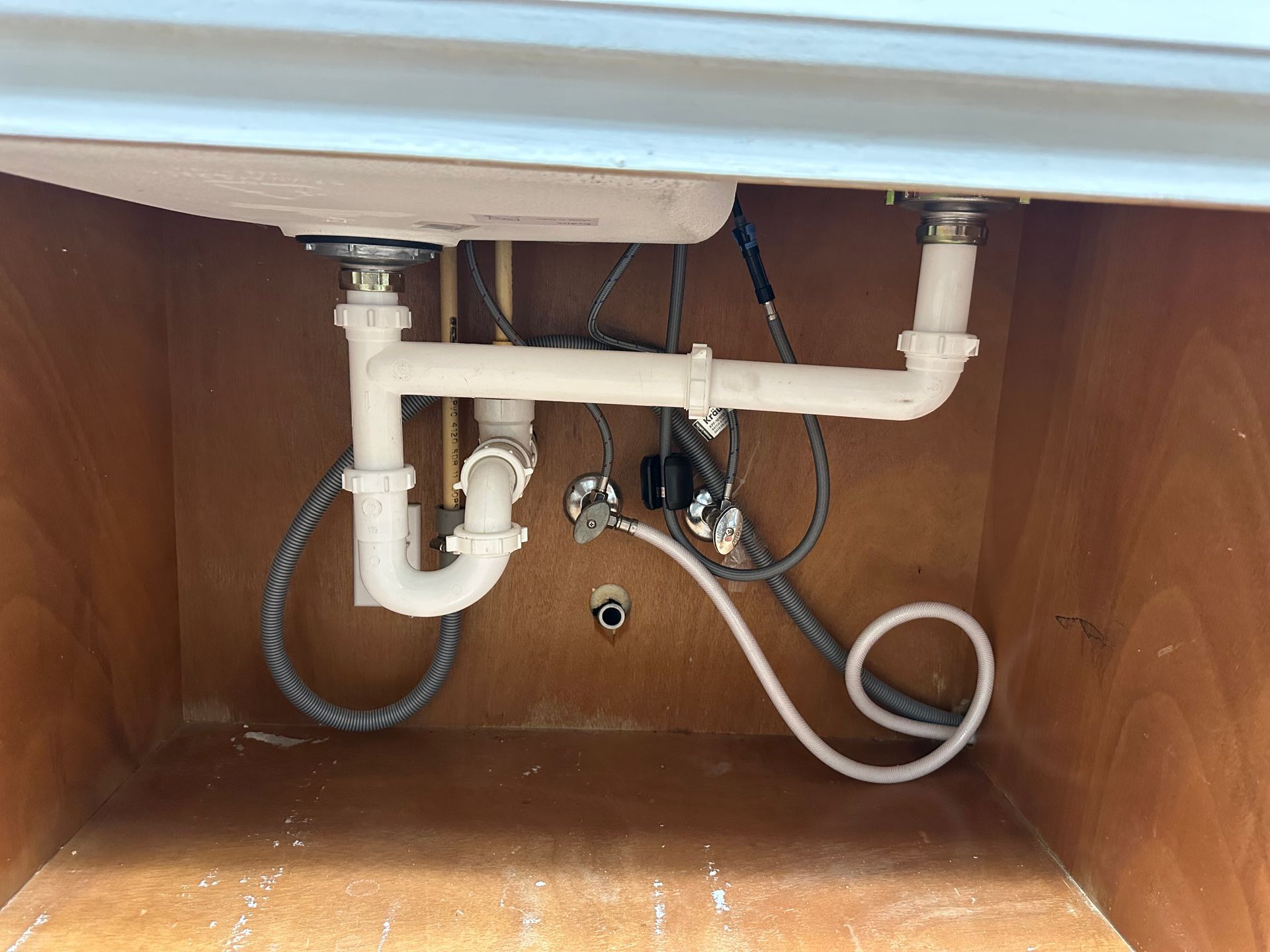 Underside of a bathroom sink with white pipes and plumbing against a brown cabinet.