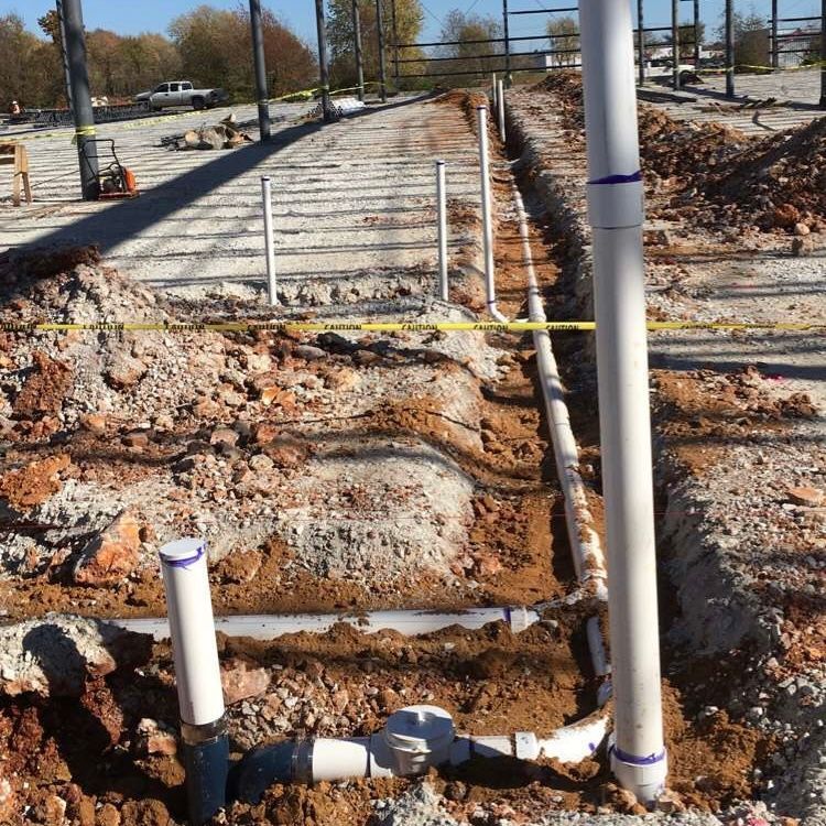 Construction site with white PVC pipes laid in trenches, brown dirt.