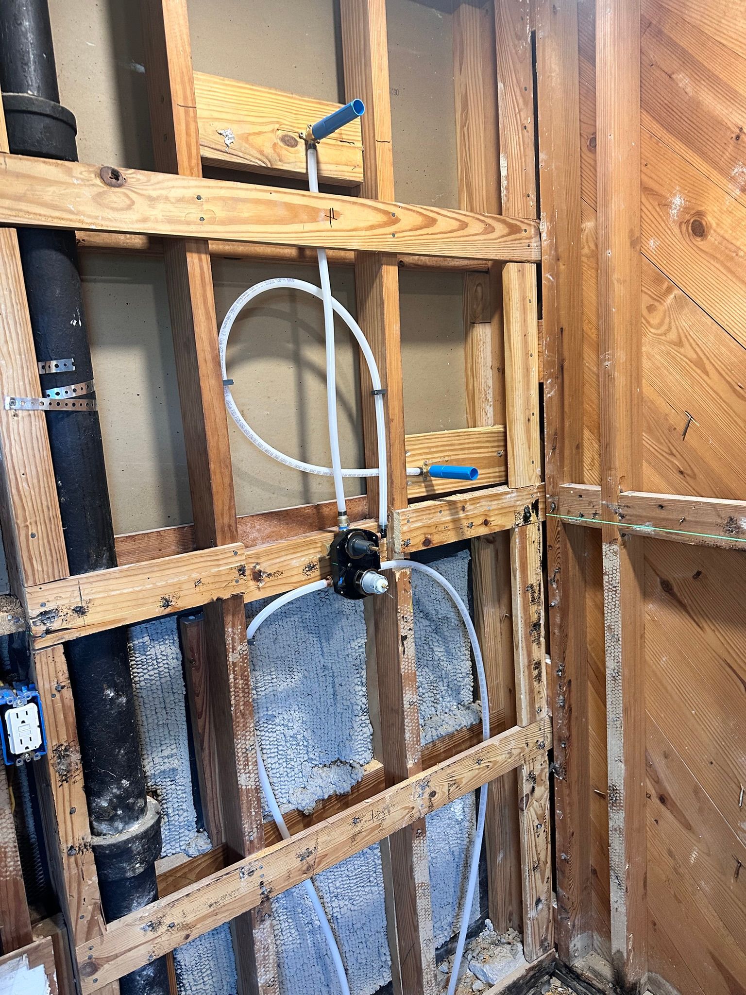 Interior view of a bathroom's exposed wooden frame, plumbing, and black pipes.