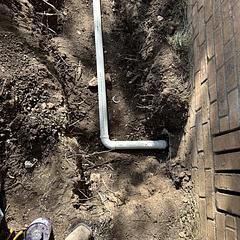White PVC pipe in trench near brick wall, soil.