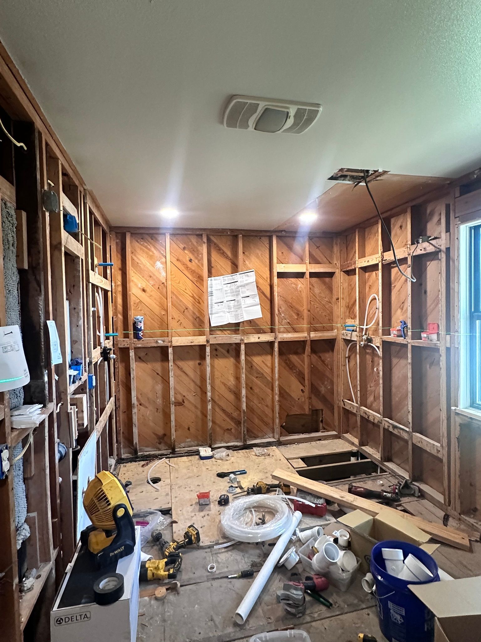 Interior room under renovation, wooden studs exposed, debris on floor, tools and materials scattered.