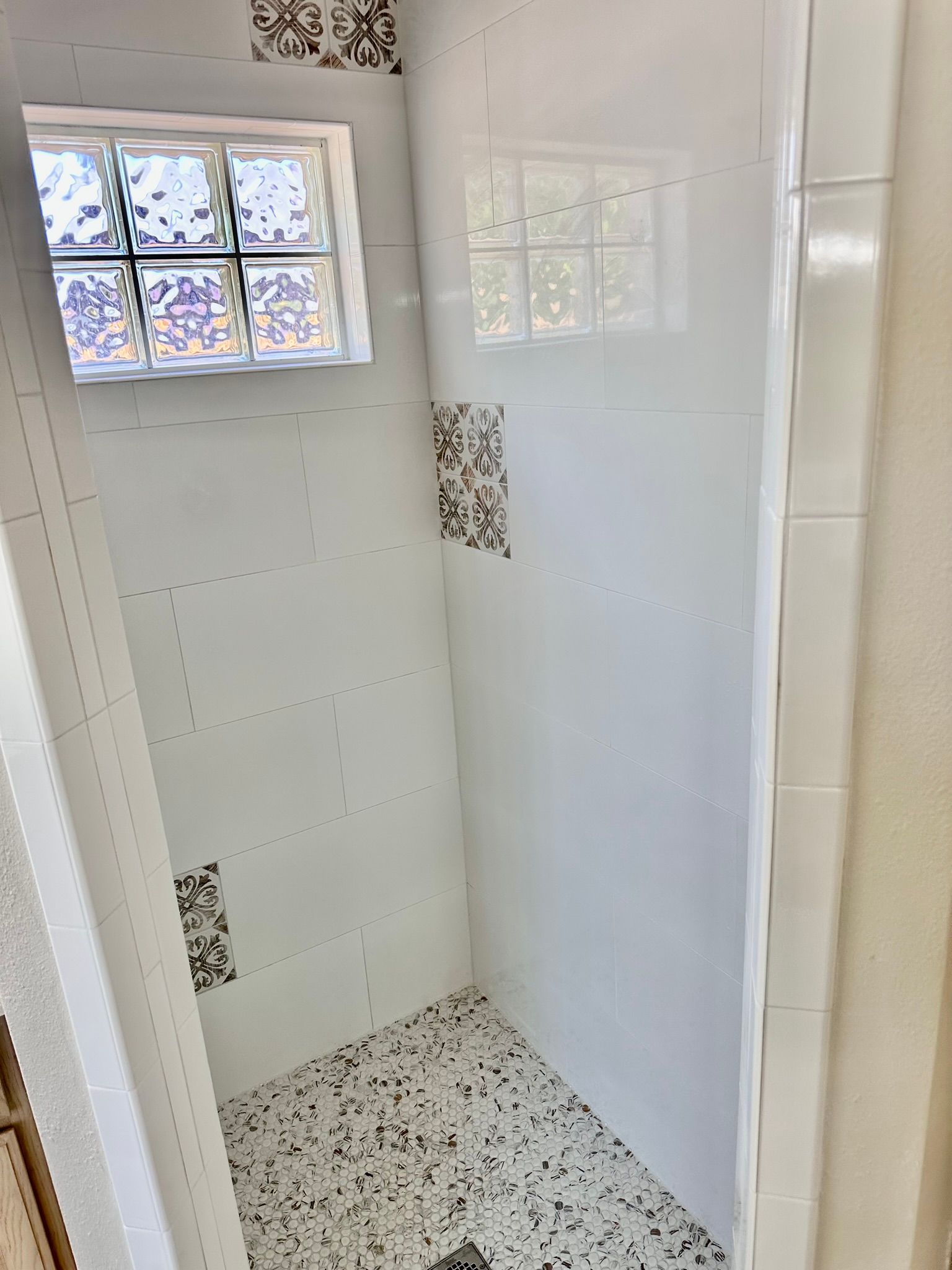 White tiled shower with glass block window, patterned floor, and accent tiles.