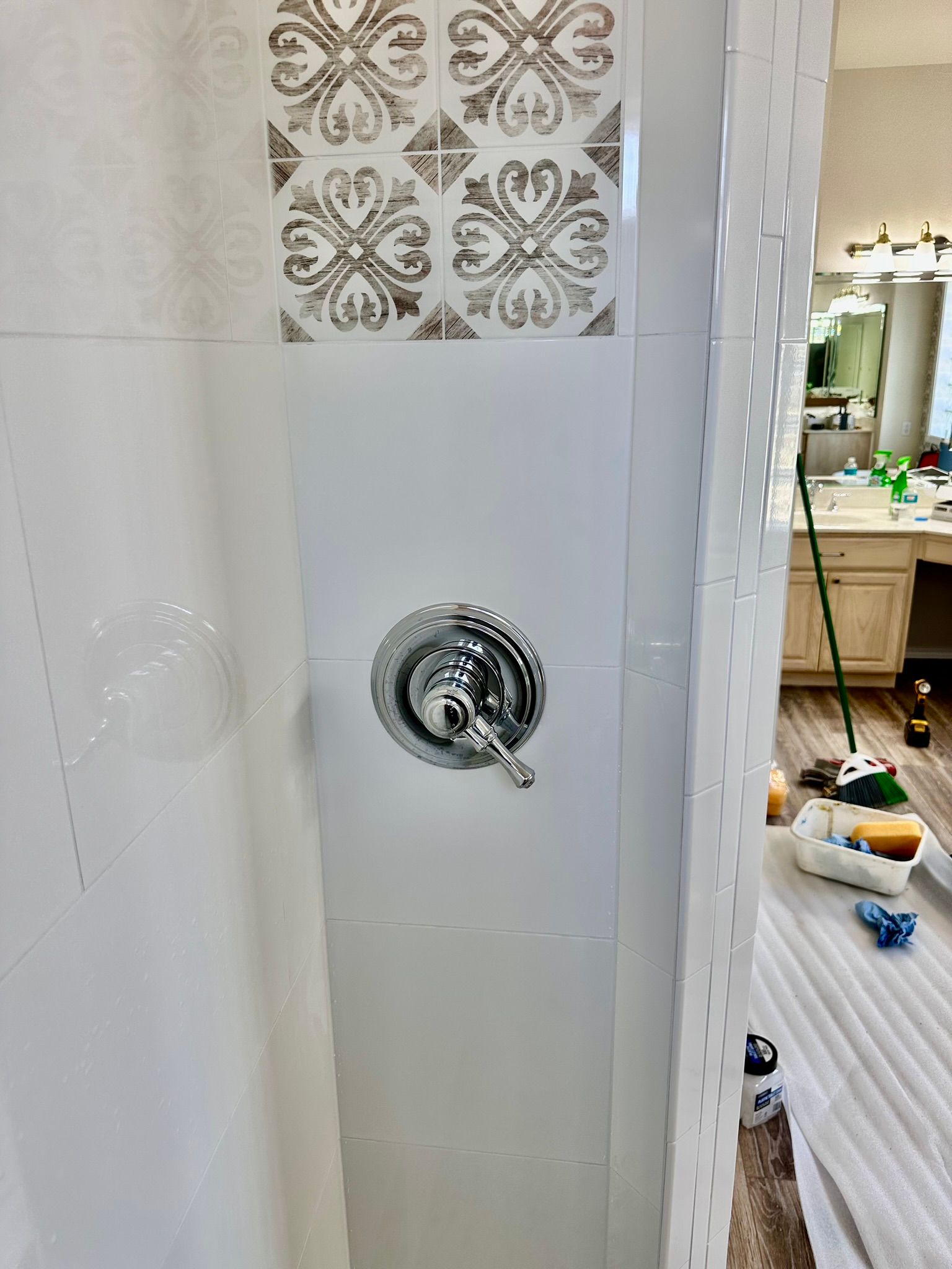 Shower with white and patterned tile, chrome faucet, and glimpse of a bathroom.