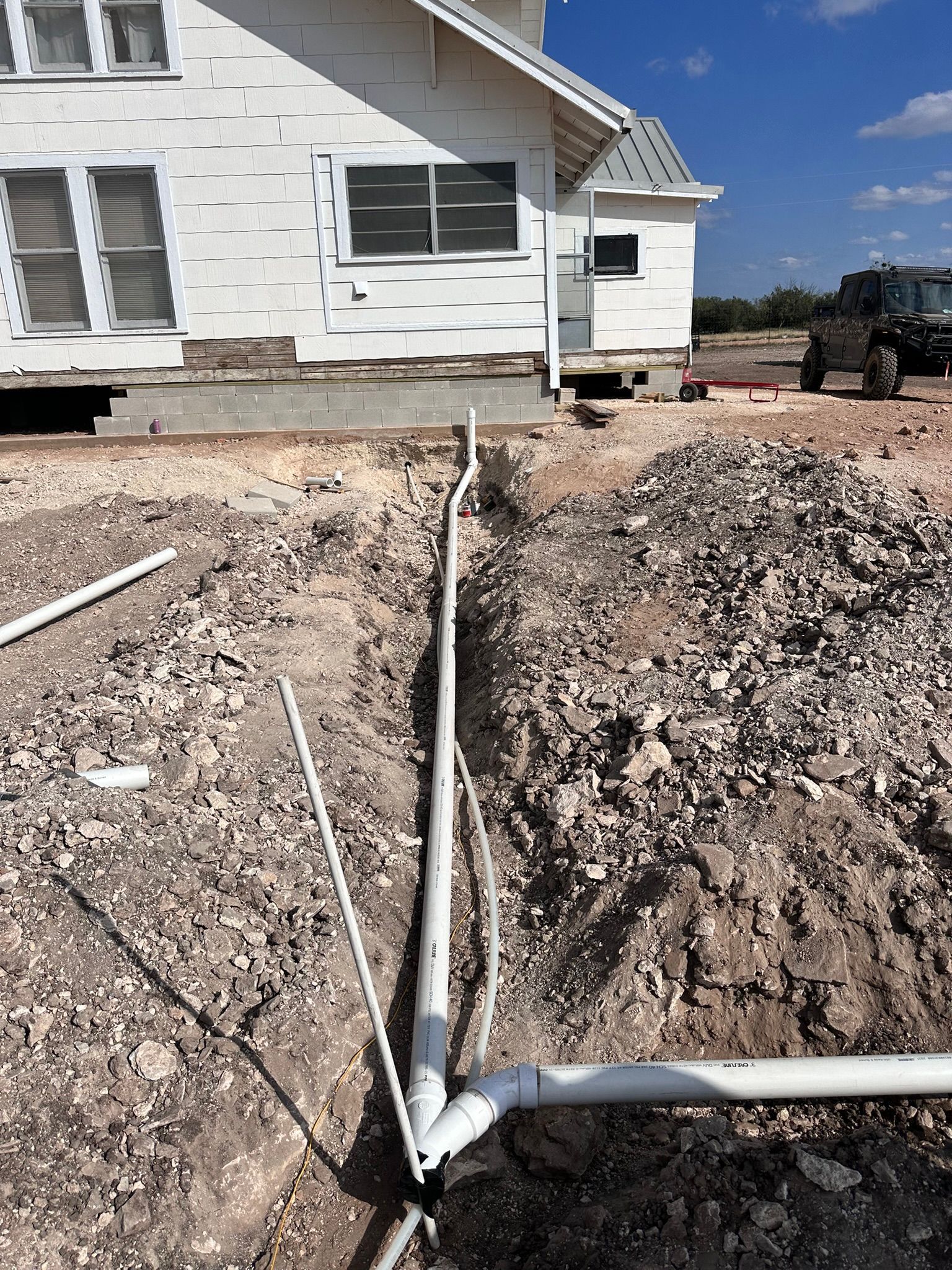 Trench dug with white PVC pipes, near a white house with some construction happening.