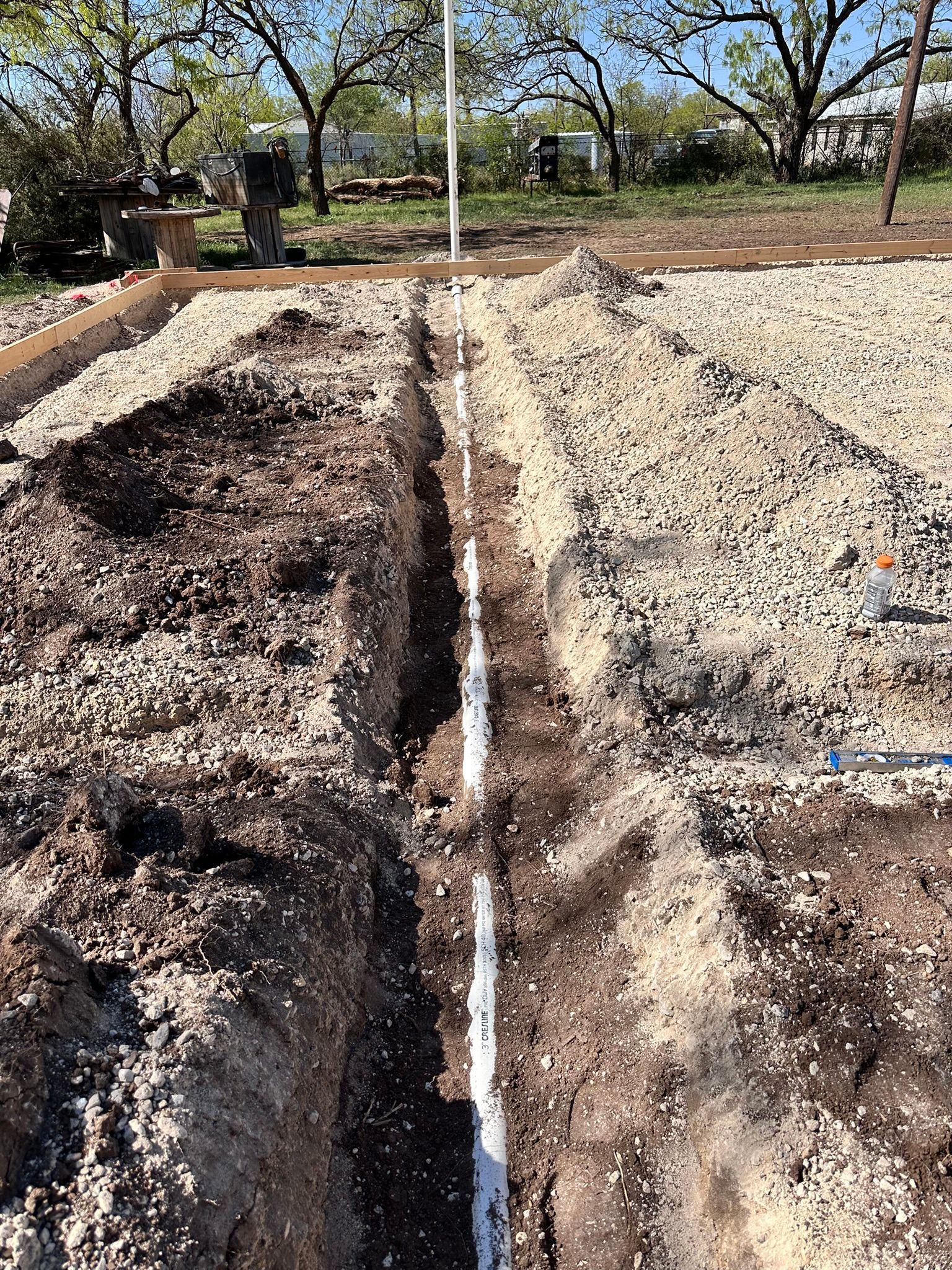 A trench with white PVC pipe installed for an irrigation system in a garden setting.