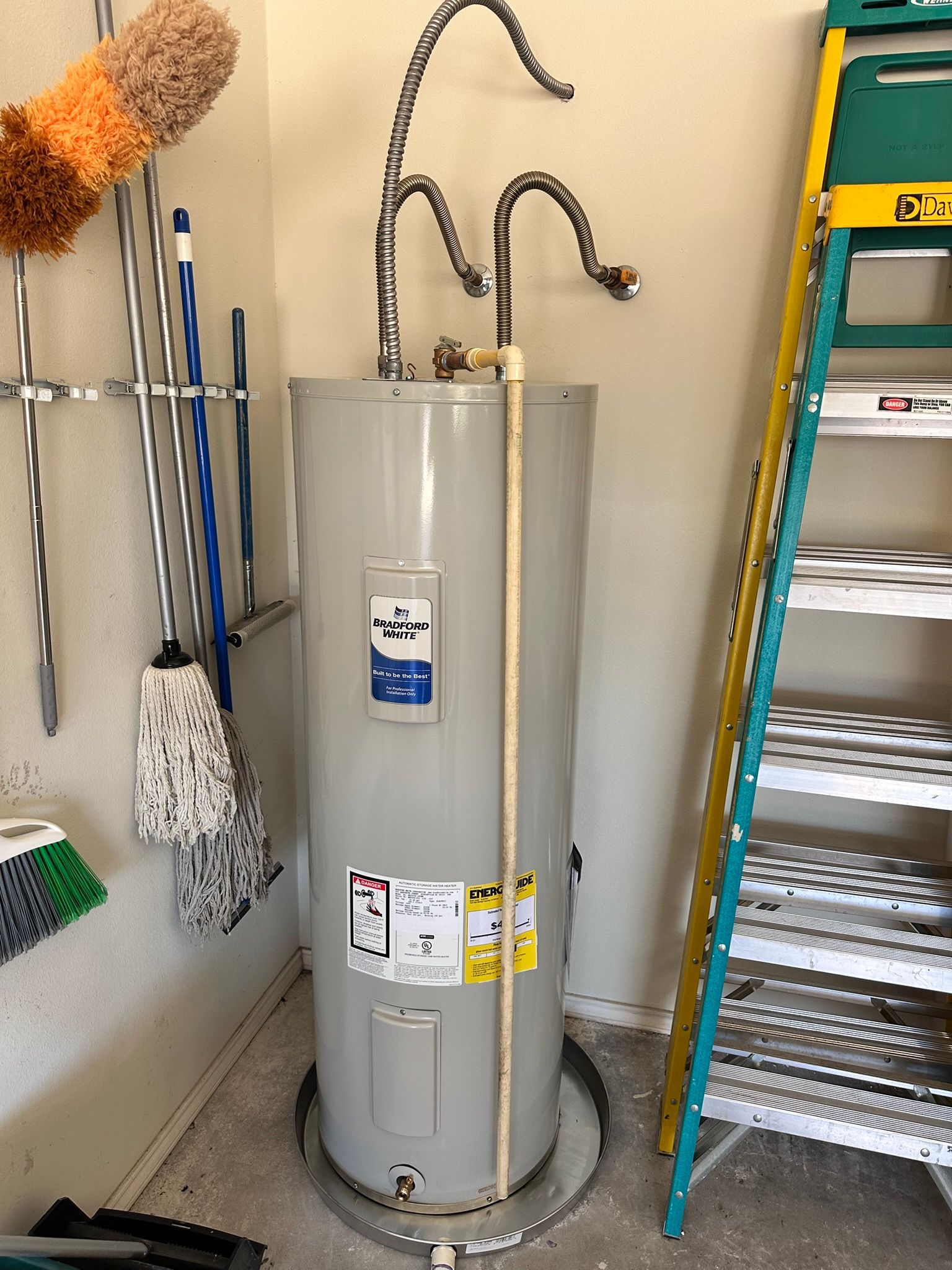 Water heater in a corner with cleaning supplies, ladder, and exposed plumbing.