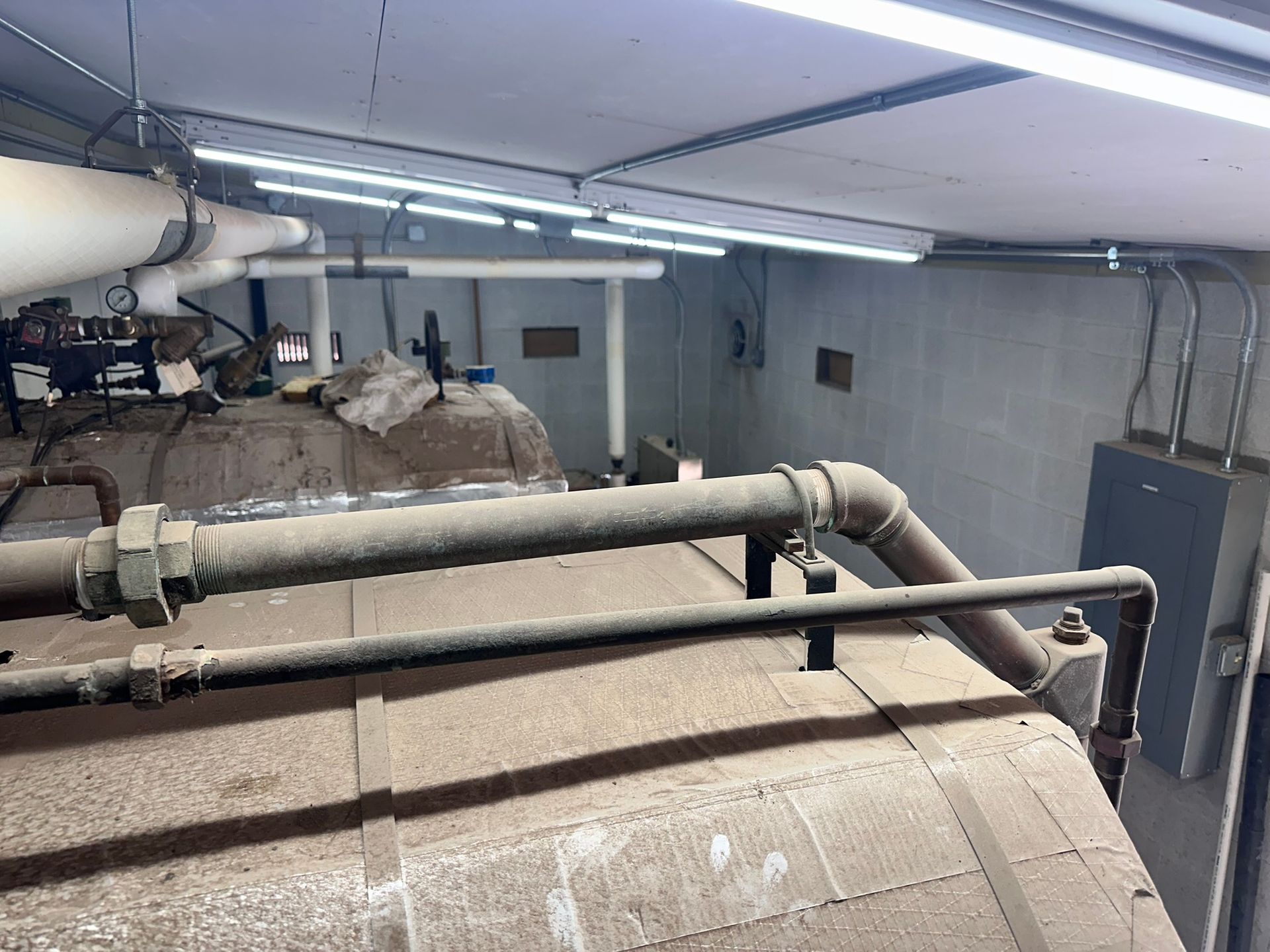 Industrial equipment in a utility room, including pipes, tanks, and electrical components, all covered in dust.