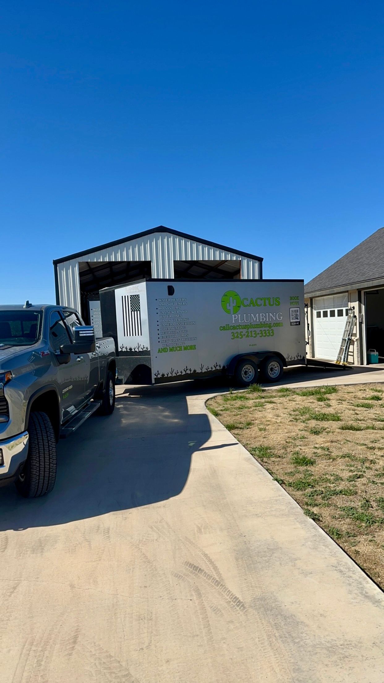 Truck pulling trailer with business logo parked near a metal building and house, sunny day.