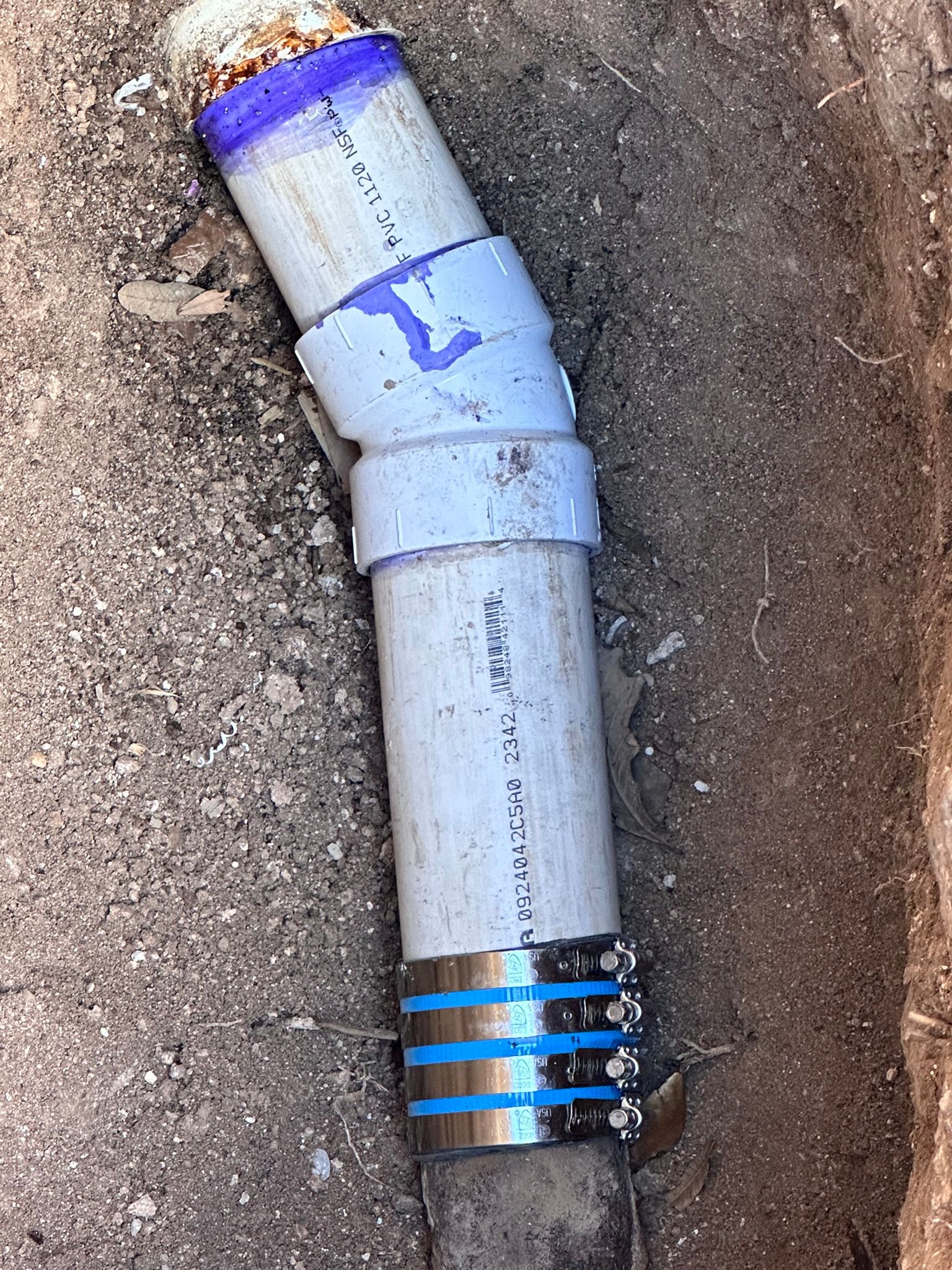 PVC plumbing pipe with angled joint, partly buried in dirt.