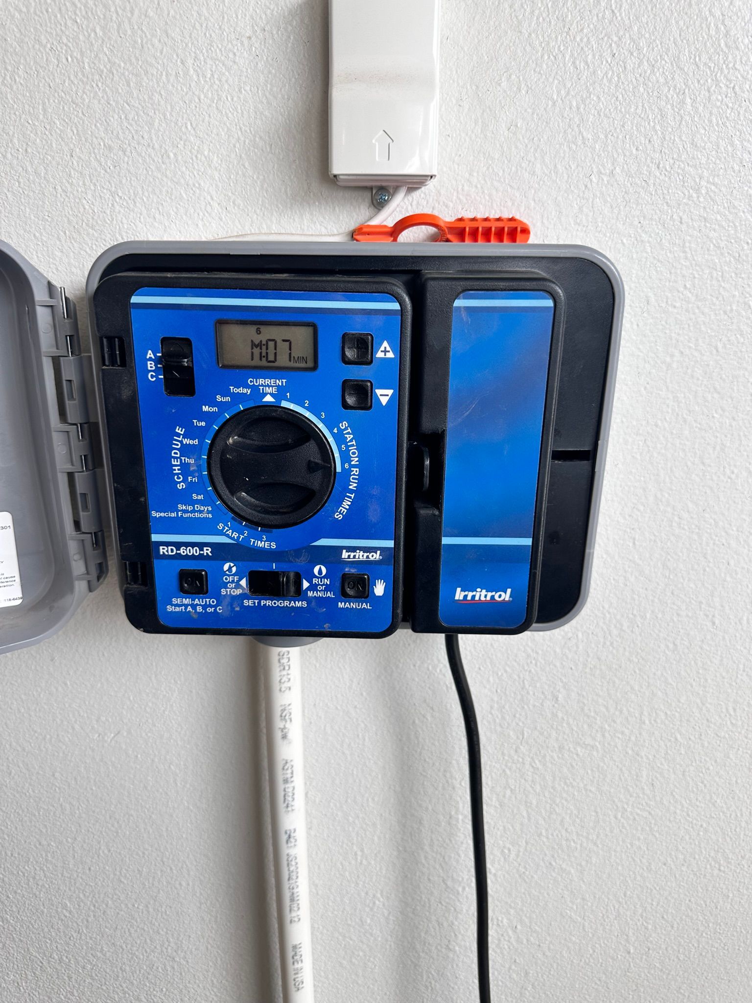 Blue irrigation system control panel mounted on a wall with a white conduit below.