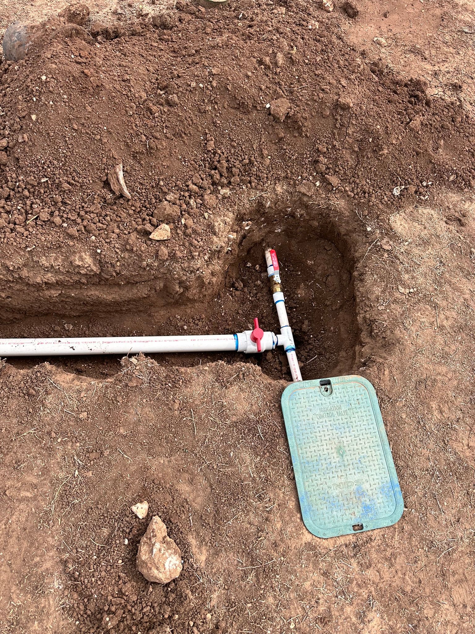 White pipes and red valves in a dirt trench near a blue rectangular cover.