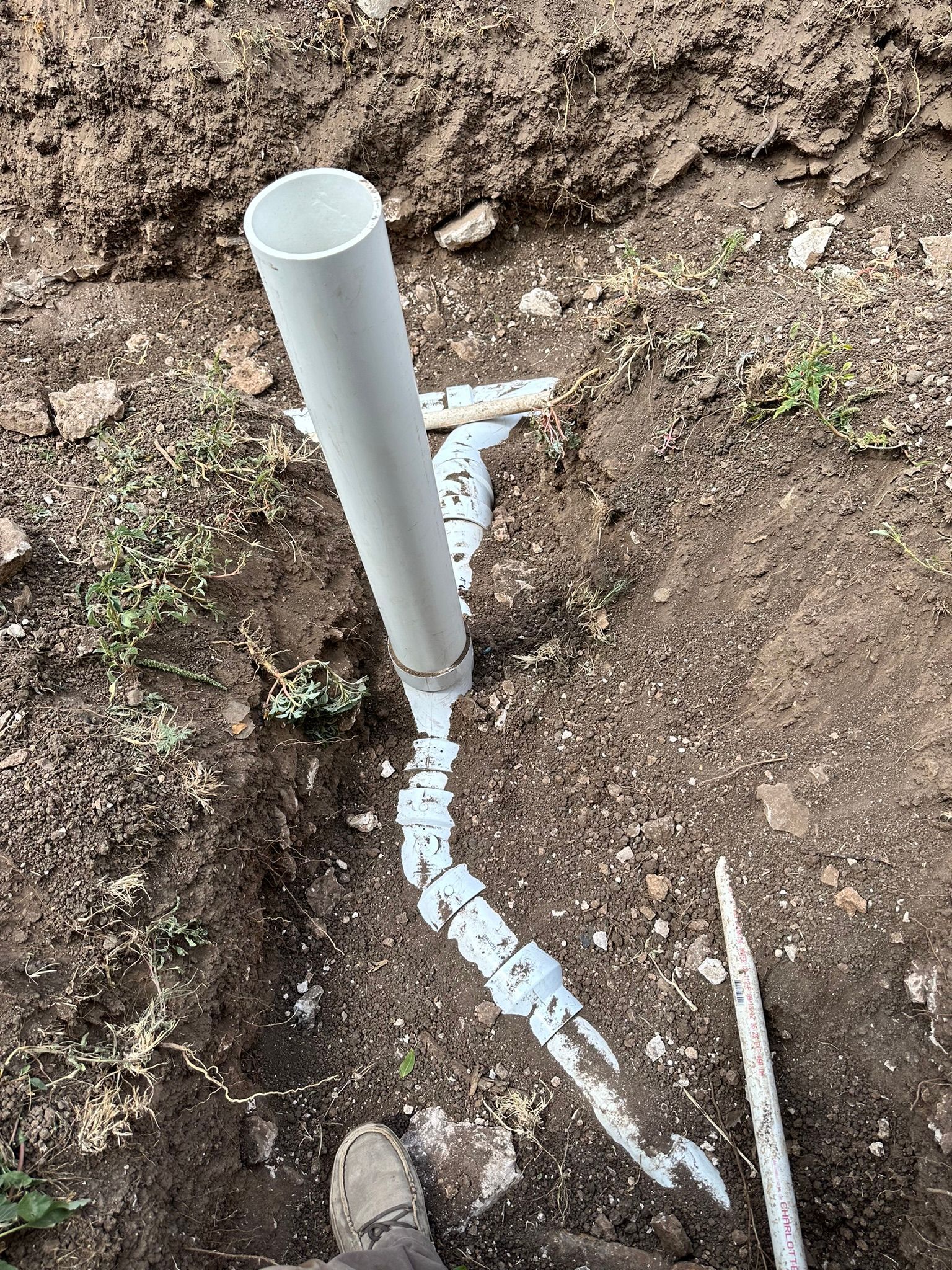 PVC pipes partially buried in dirt, with a long vertical pipe extending upwards.
