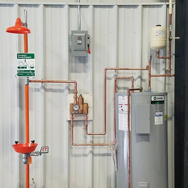 Emergency safety shower and eye wash station with a water heater and plumbing, on a metal wall.