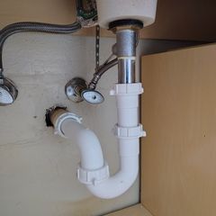 White sink drain pipes under a sink.  Metal faucet pipes also present.