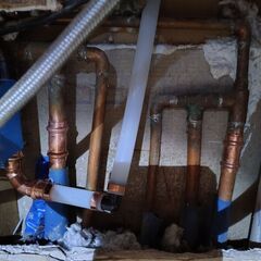 Copper pipes and fittings in a wall cavity, with white plastic piping, blue tape and background debris.
