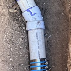 White PVC pipes with blue fittings in a dirt trench.
