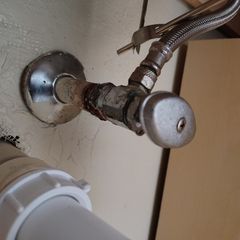 Close-up of a corroded water shut-off valve with a flexible hose connected under a sink.