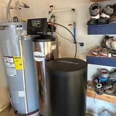 Water softener and tank system in a garage, with a water heater and shelving with shoes.