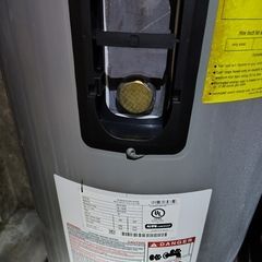 Close-up of a water heater with a pressure relief valve. Yellow warning label visible.