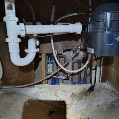 Plumbing under a sink: garbage disposal, pipes, P-trap, electrical outlet, and water lines in a cabinet.