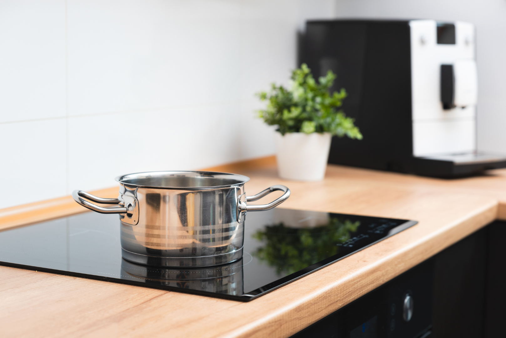 Stainless steel pot on a black stovetop in a modern kitchen with a coffee machine and small plant nearby