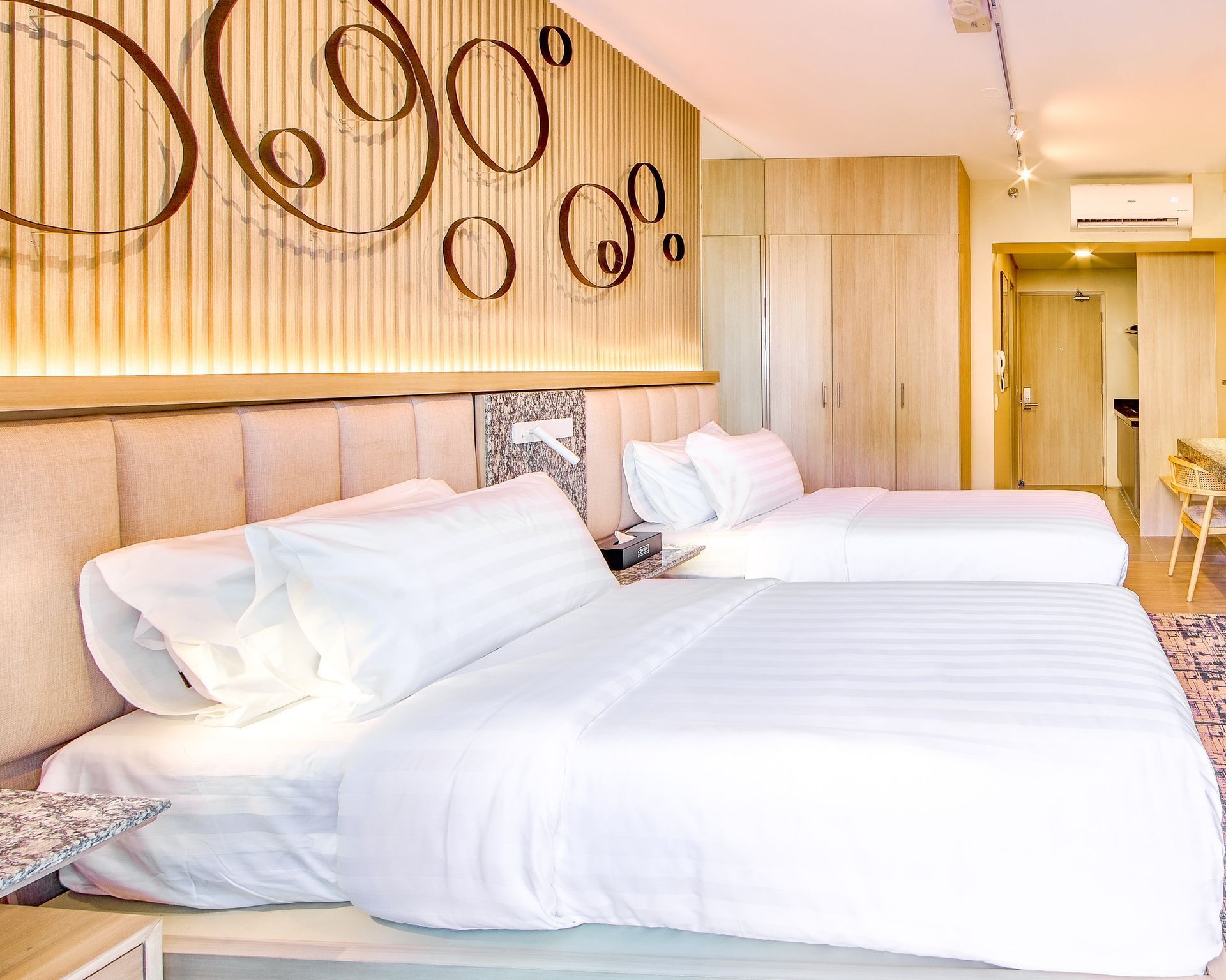 Bright modern hotel room with two white beds, wood accents, and circular wall decor