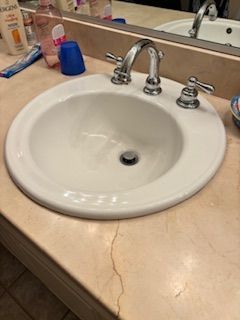 A bathroom sink with silver faucets set into a light-colored vanity countertop that has a noticeable crack in front.