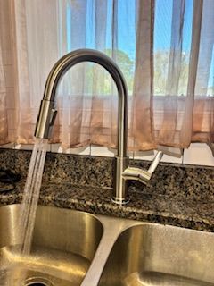 A stainless steel kitchen faucet with a pull-down sprayer running water over a double stainless steel sink.