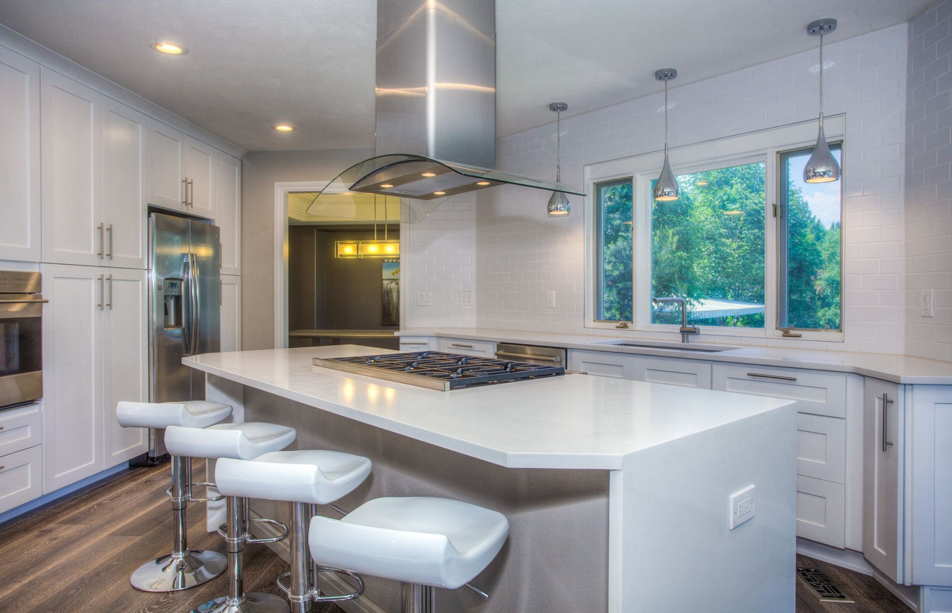 A modern, brightly lit kitchen featuring a white center island with stools, stainless steel appliances, and a range hood.