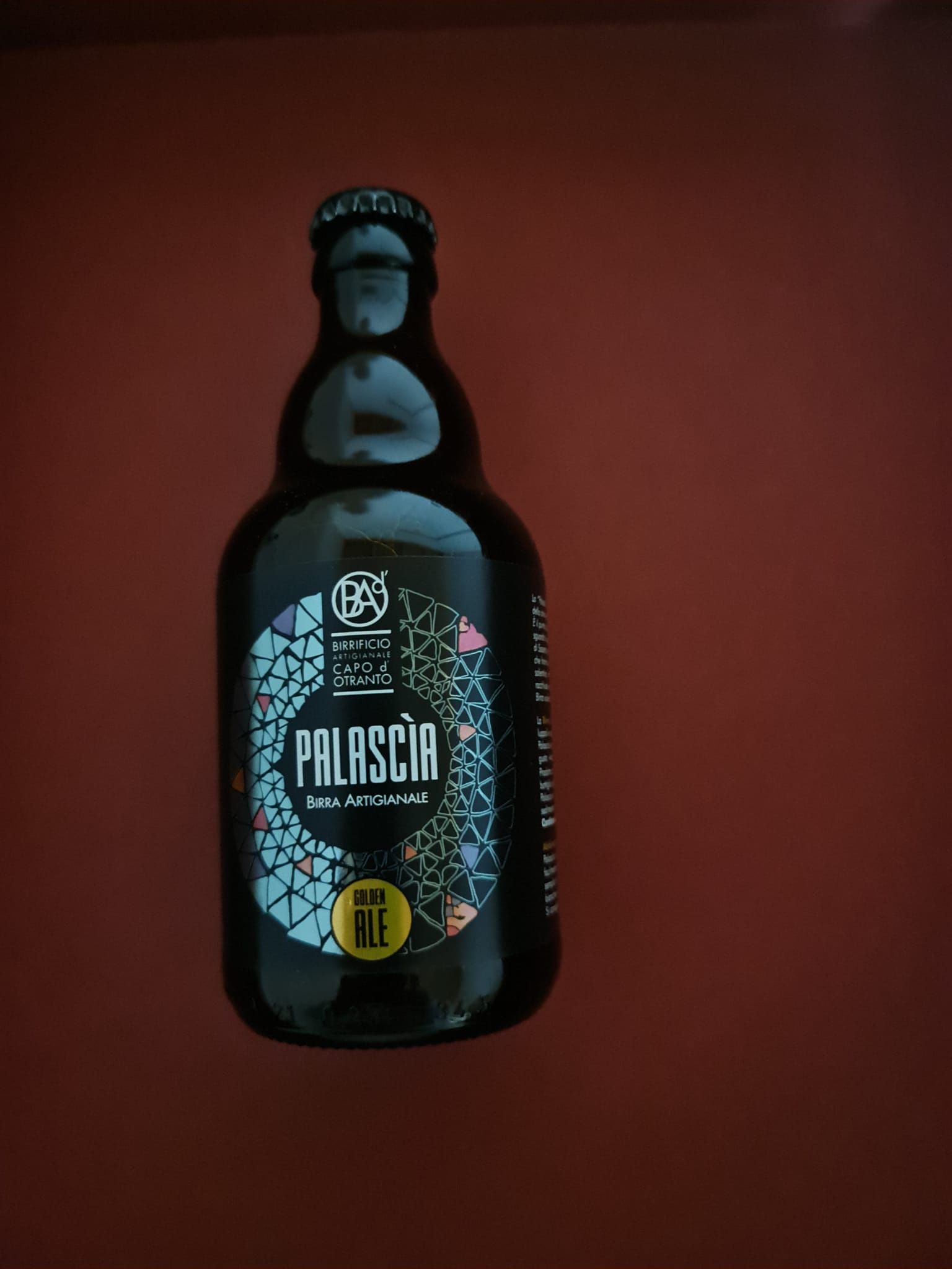 Une bouteille de bière Palmscia est posée sur une surface rouge.