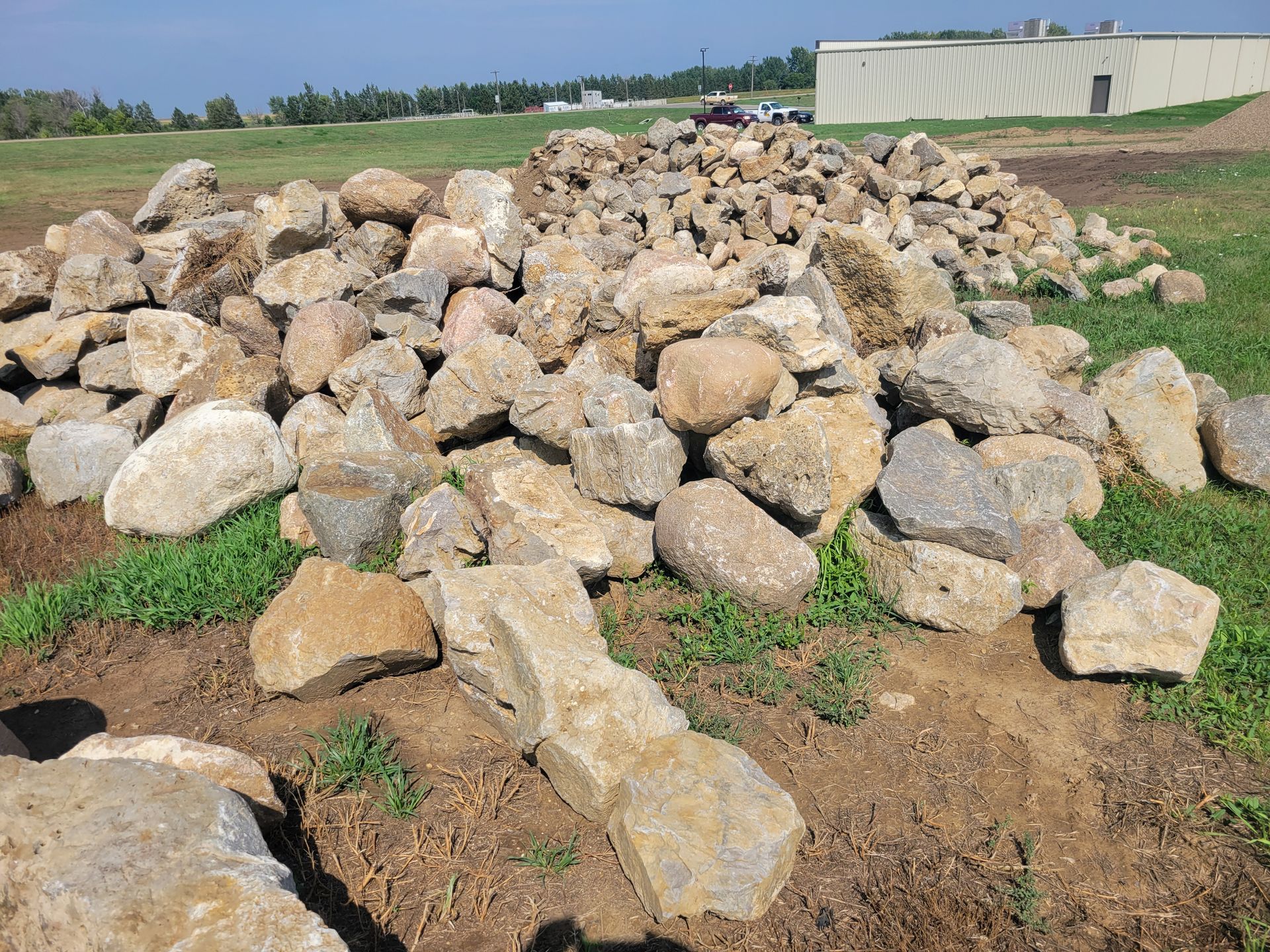 Pile of light-colored rocks in a grassy field, with a building in the background.