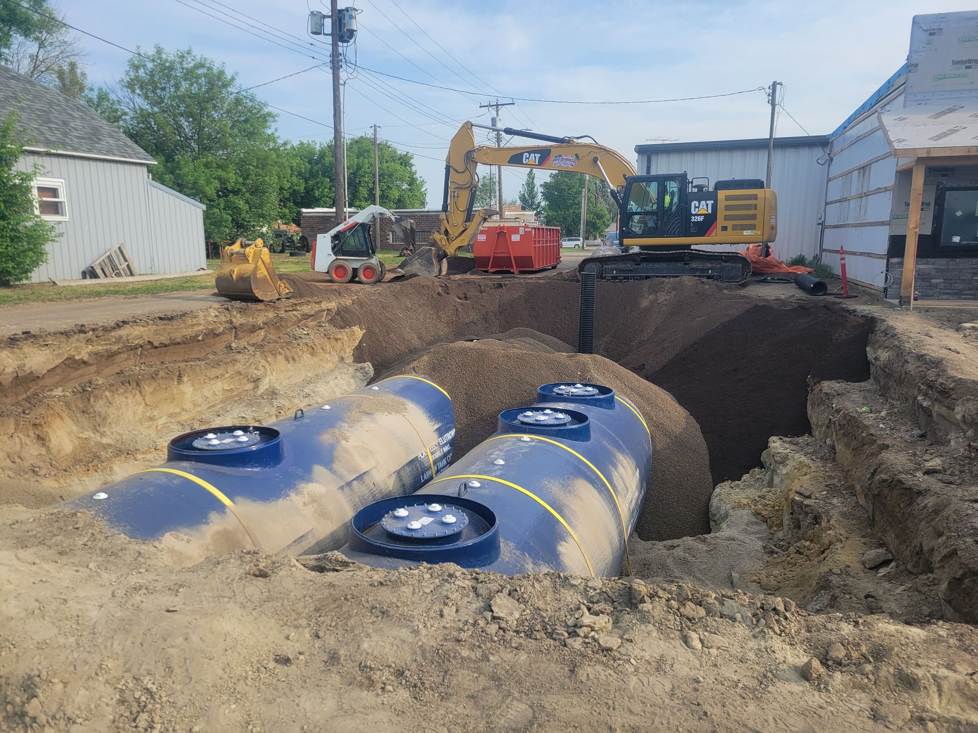 Construction site with blue tanks in a trench, excavators working.